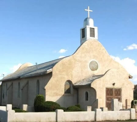 Historic white adobe mission church in rural New Mexico under blue sky