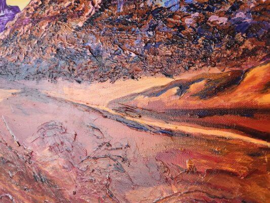 Close-up texture of Clark Sheppard’s Monument Valley painting showing layered ochres, violets, and sculpted brushstrokes that create a rugged desert floor with dimensional, glowing Southwest colors.